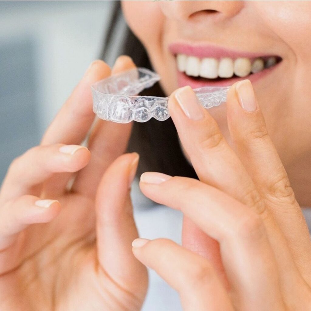 Woman holding a clear aligner next to her smile