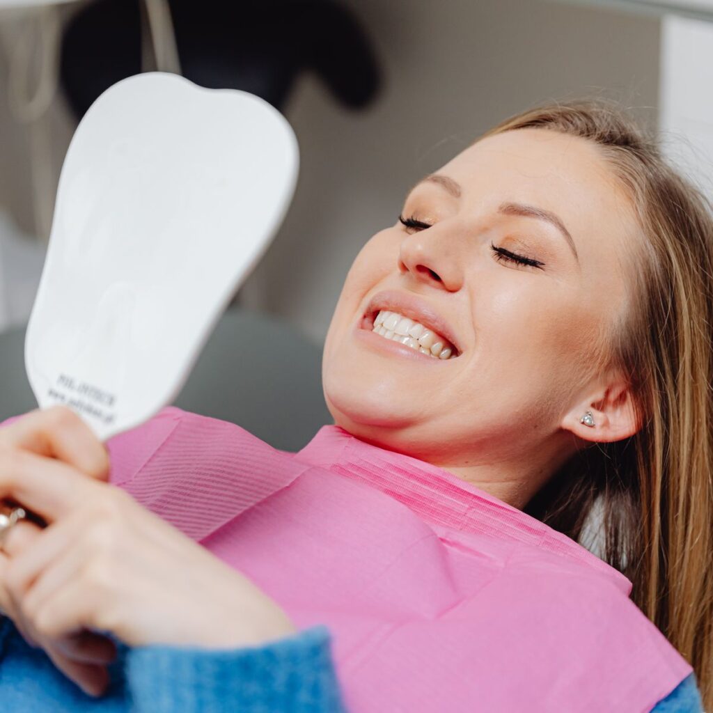 Woman smiling at her new smile in a mirror after cosmetic dentistry